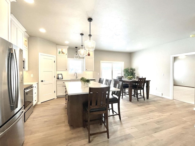 kitchen featuring stainless steel appliances, sink, decorative light fixtures, white cabinetry, and a kitchen island