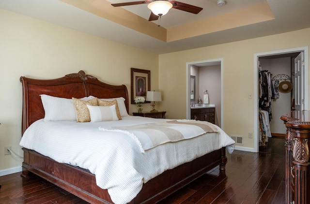 bedroom with baseboards, a spacious closet, a tray ceiling, and dark wood-type flooring