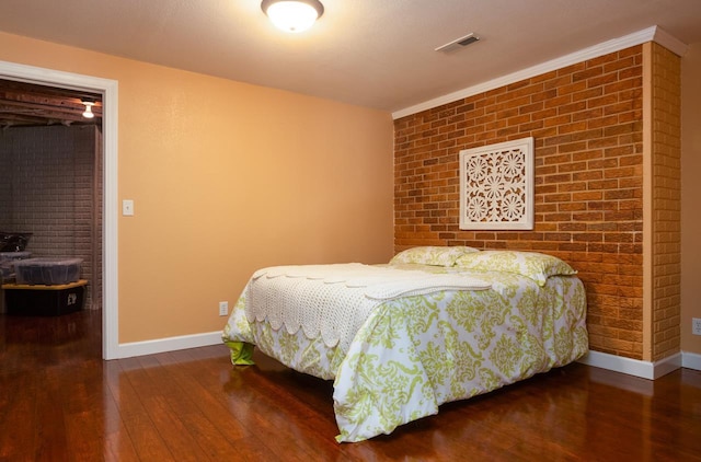 bedroom featuring dark wood-style flooring, visible vents, baseboards, and brick wall