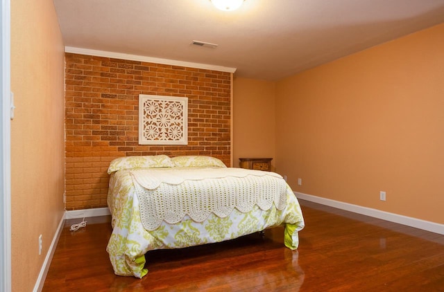 bedroom featuring brick wall, dark wood finished floors, visible vents, and baseboards