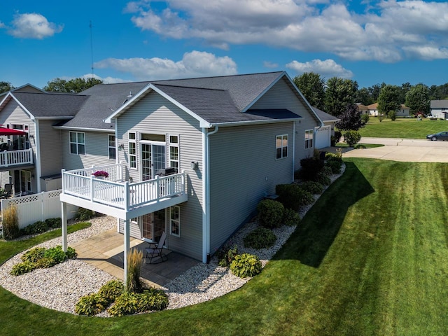 back of house featuring a deck, a patio, a shingled roof, and a lawn