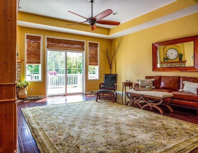 living room with visible vents, baseboards, ceiling fan, wood finished floors, and a tray ceiling