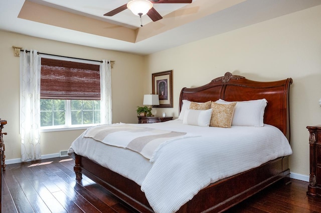 bedroom with a tray ceiling, dark wood finished floors, baseboards, and ceiling fan