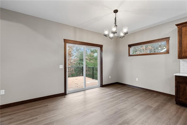 unfurnished room with a notable chandelier, light wood finished floors, and baseboards