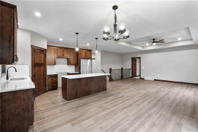 kitchen featuring a center island, a tray ceiling, visible vents, freestanding refrigerator, and a sink