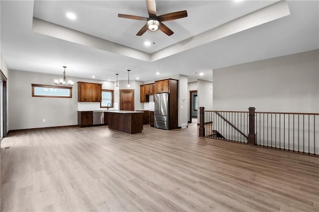 kitchen with stainless steel appliances, open floor plan, a center island, light wood finished floors, and a raised ceiling