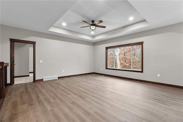 spare room with baseboards, visible vents, a raised ceiling, and light wood-style flooring