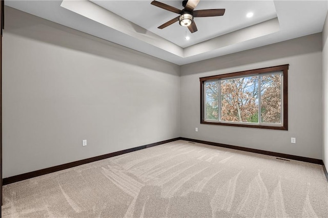 unfurnished room featuring visible vents, baseboards, a raised ceiling, light colored carpet, and ceiling fan