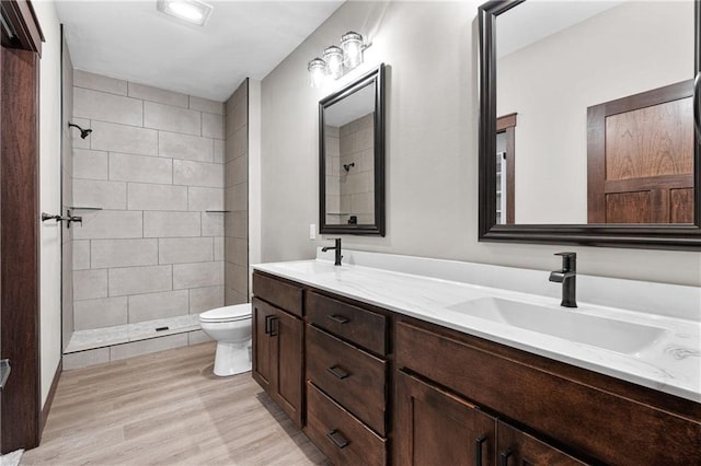 full bath with toilet, double vanity, a tile shower, and a sink