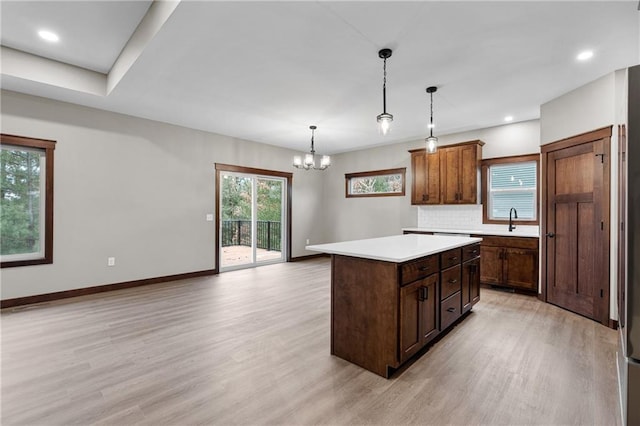 kitchen featuring light wood finished floors, a kitchen island, backsplash, and a sink