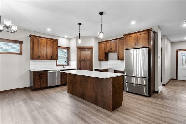 kitchen with appliances with stainless steel finishes, a center island, light wood-style floors, and tasteful backsplash