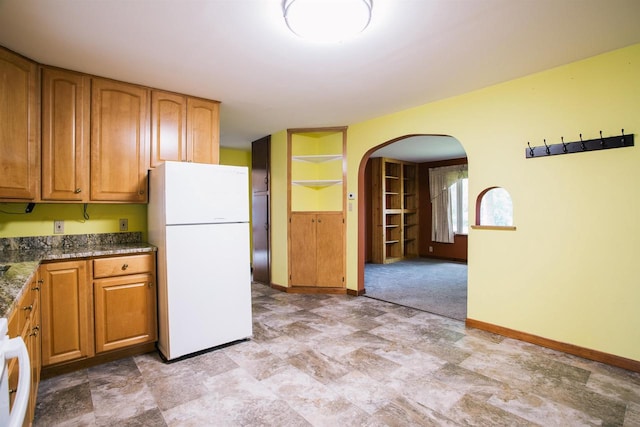 kitchen featuring dark stone countertops, light tile patterned flooring, and white fridge