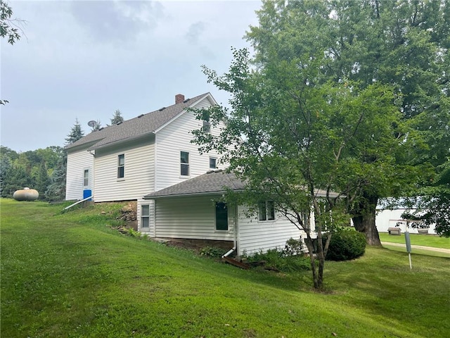 view of side of home with roof with shingles, a lawn, and a chimney