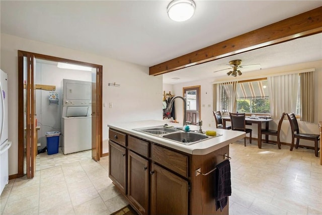 kitchen featuring stacked washer and dryer, an island with sink, a sink, light countertops, and beam ceiling