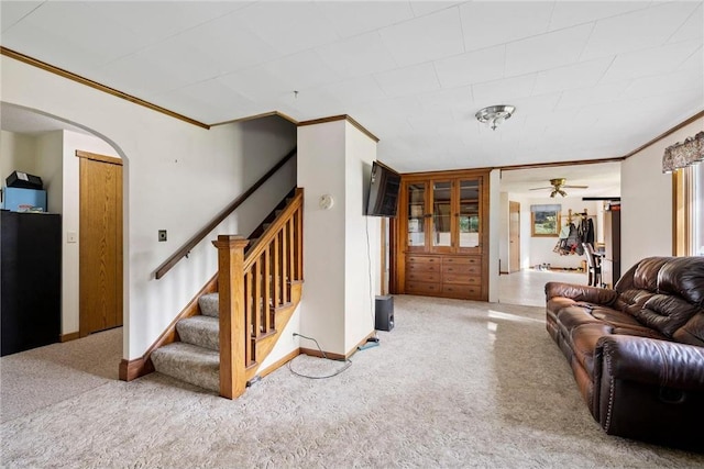 living area with baseboards, arched walkways, a ceiling fan, stairway, and ornamental molding