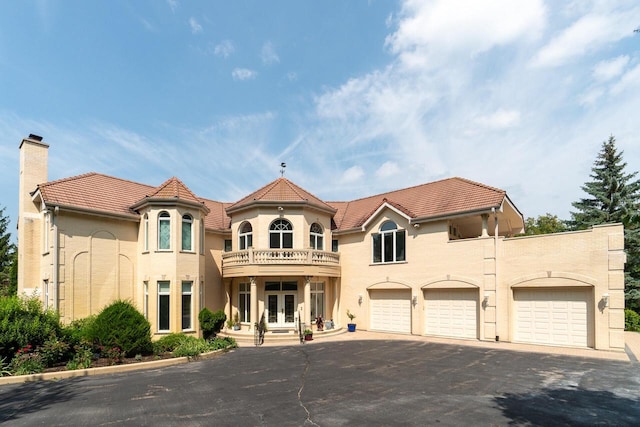 view of front facade featuring aphalt driveway, french doors, a chimney, a balcony, and a tiled roof