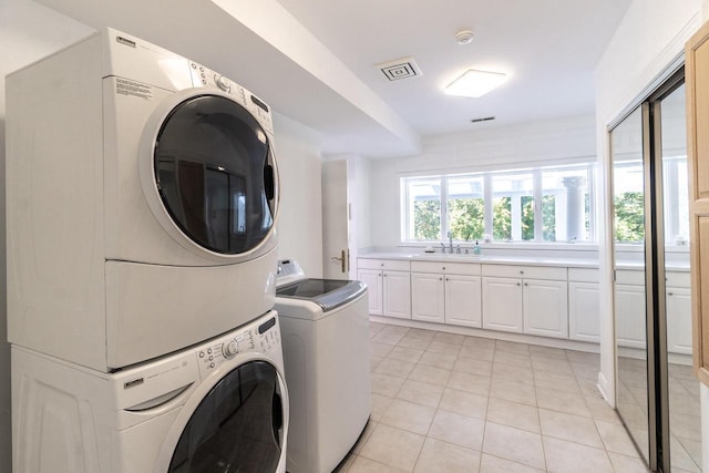 laundry area with light tile patterned floors, laundry area, visible vents, stacked washing maching and dryer, and a sink