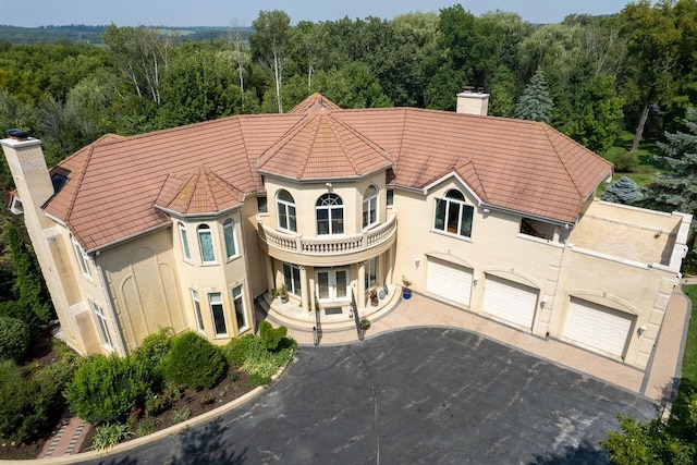 view of front of property with a garage, a forest view, a chimney, and driveway