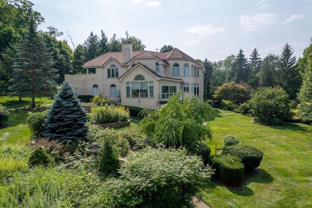 rear view of house featuring a chimney, a lawn, and stucco siding