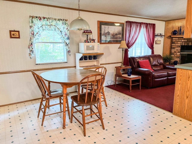 dining area with a brick fireplace, crown molding, and light floors