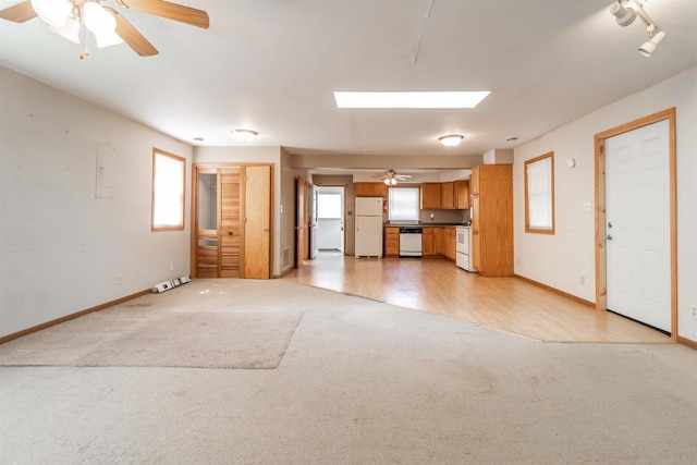 unfurnished living room featuring ceiling fan, light wood-type flooring, and a skylight