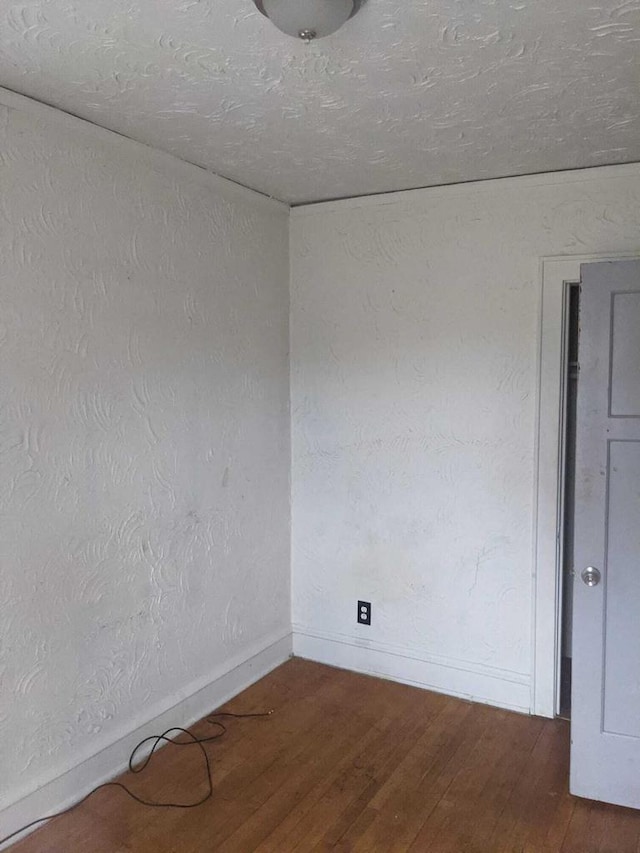 empty room with wood-type flooring, a textured wall, and baseboards