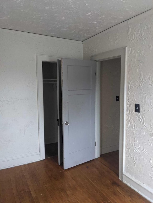 unfurnished bedroom featuring baseboards, hardwood / wood-style floors, and a textured wall