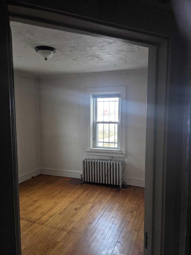 empty room with radiator, a textured ceiling, baseboards, and hardwood / wood-style flooring