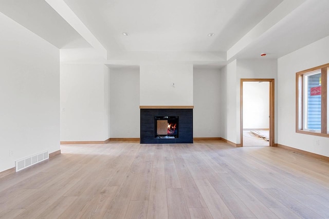 unfurnished living room featuring light wood-type flooring and a tiled fireplace