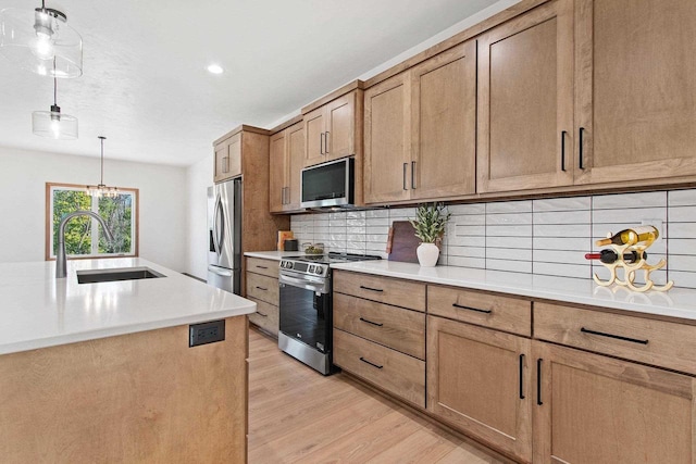 kitchen featuring sink, decorative light fixtures, stainless steel appliances, light hardwood / wood-style floors, and decorative backsplash