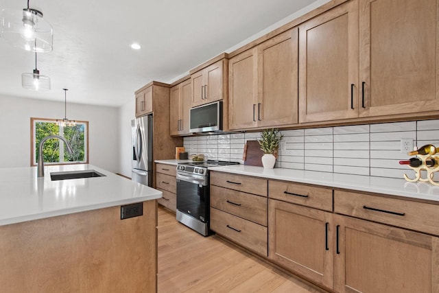 kitchen featuring backsplash, pendant lighting, stainless steel appliances, light wood-type flooring, and sink