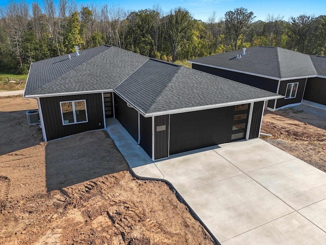 ranch-style house with central AC unit, an attached garage, a shingled roof, and concrete driveway