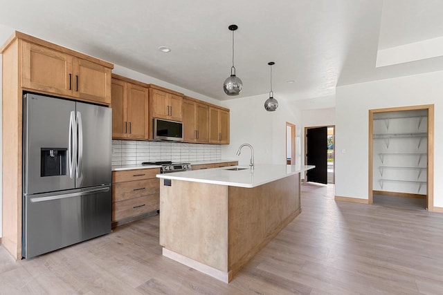 kitchen with a center island with sink, pendant lighting, stainless steel appliances, and light hardwood / wood-style flooring