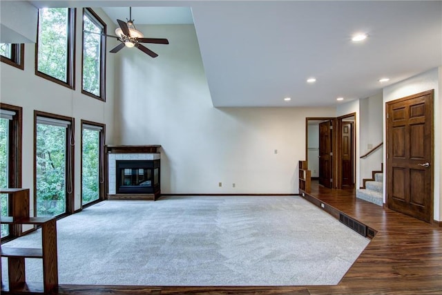 unfurnished living room featuring a high ceiling, wood-type flooring, a fireplace, and ceiling fan