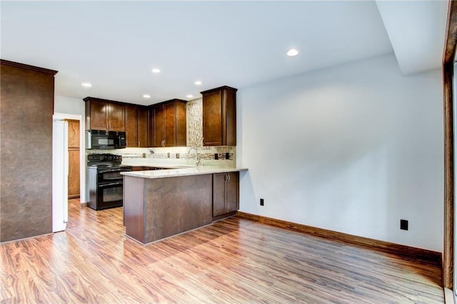 kitchen with black appliances, kitchen peninsula, sink, decorative backsplash, and light hardwood / wood-style floors