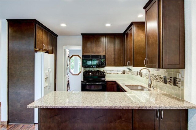 kitchen featuring black appliances, light stone counters, kitchen peninsula, sink, and hardwood / wood-style flooring