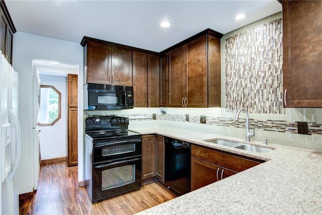 kitchen featuring black appliances, hardwood / wood-style floors, tasteful backsplash, sink, and light stone counters