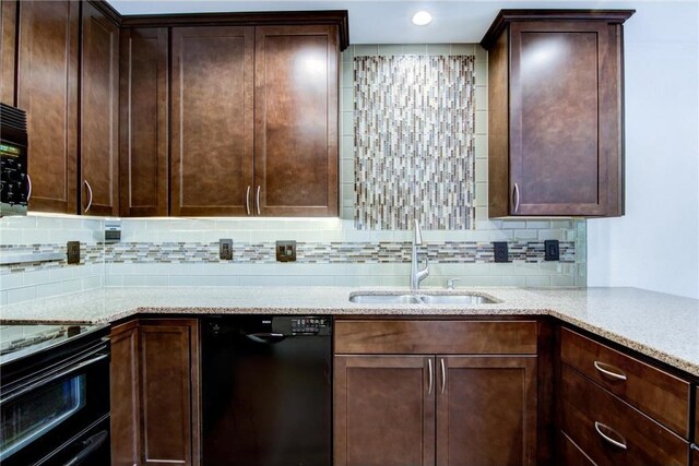 kitchen featuring black appliances, light stone counters, decorative backsplash, and sink