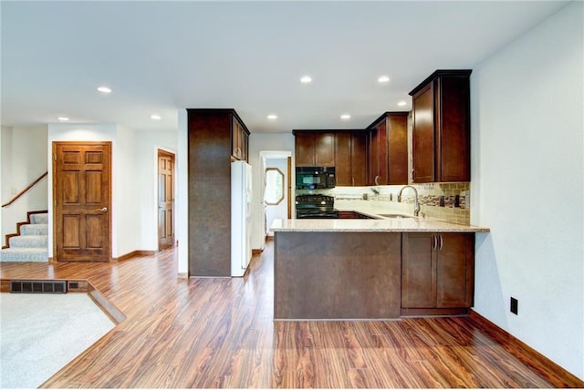 kitchen featuring black appliances, tasteful backsplash, kitchen peninsula, sink, and hardwood / wood-style flooring