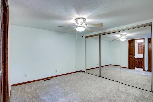 unfurnished bedroom featuring a textured ceiling, light colored carpet, ceiling fan, and a closet