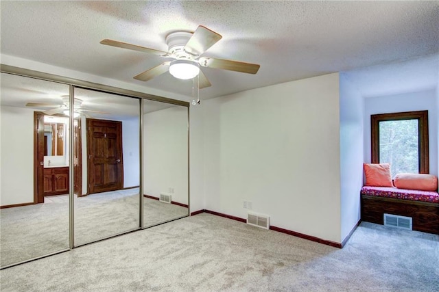 unfurnished bedroom with a textured ceiling, light colored carpet, ceiling fan, and a closet