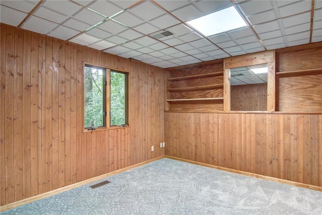 carpeted empty room featuring a paneled ceiling and wood walls