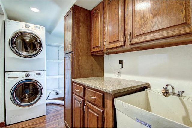 clothes washing area featuring cabinets, stacked washer / drying machine, sink, and dark hardwood / wood-style floors