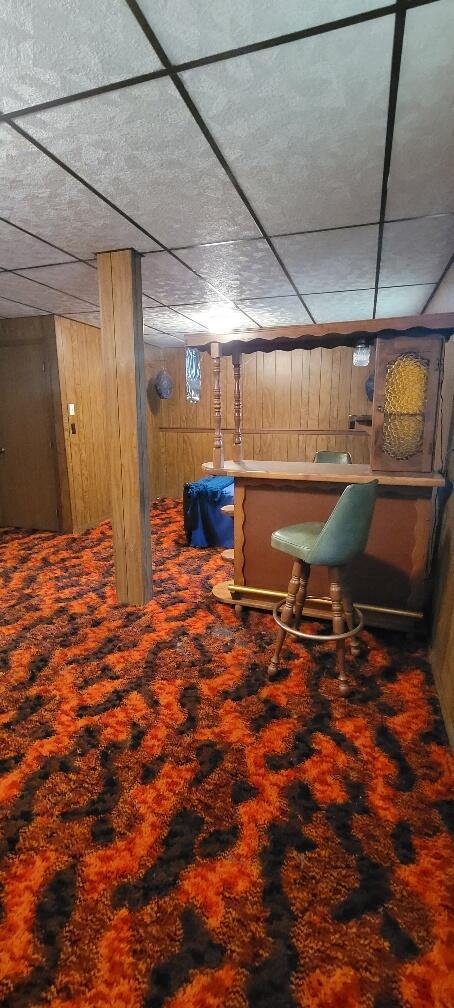 interior space featuring wood walls, bar, and a drop ceiling