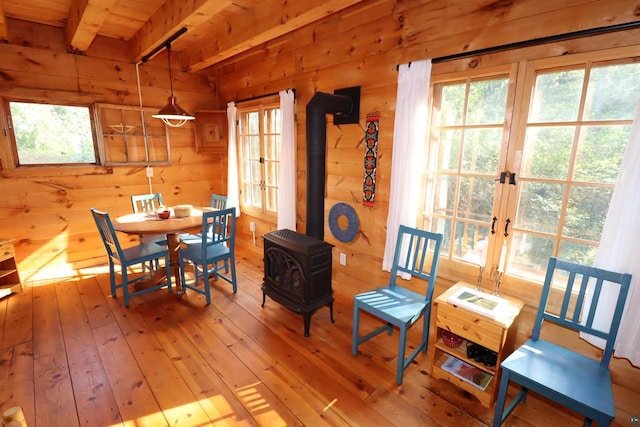 dining room with beamed ceiling, a wood stove, french doors, light hardwood / wood-style floors, and wooden walls