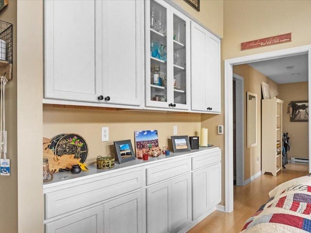 bar featuring light hardwood / wood-style flooring, baseboard heating, and white cabinets