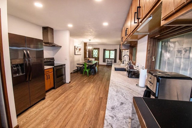 kitchen featuring light wood-type flooring, fridge with ice dispenser, black electric range oven, hanging light fixtures, and wall chimney exhaust hood