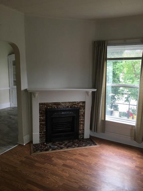 unfurnished living room with arched walkways, a tiled fireplace, and wood finished floors