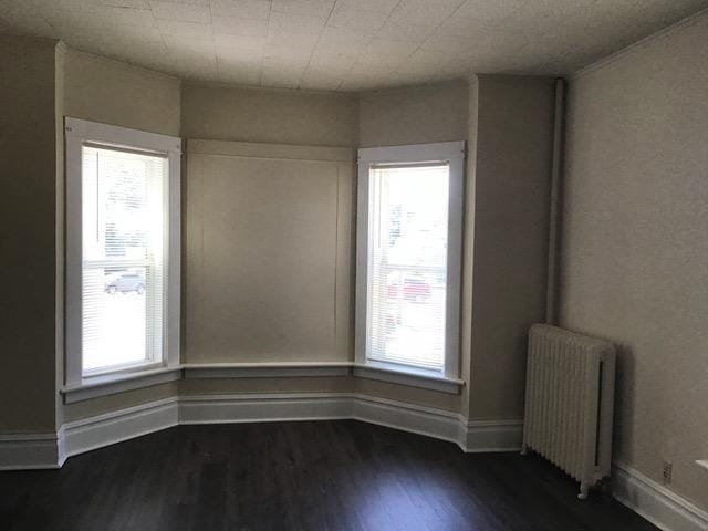 empty room with radiator, a healthy amount of sunlight, dark wood finished floors, and baseboards