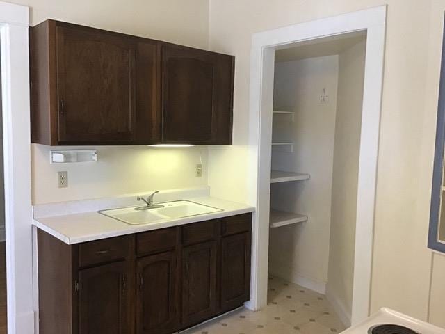 kitchen with light floors, light countertops, a sink, and dark brown cabinetry